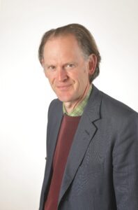 head & shoulders of a man in a grey suit and burgundy jumper