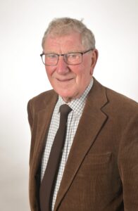 A man in a brown suit, smiling