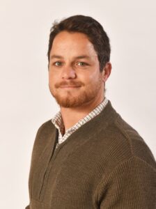 head & shoulders of a man in a brown jumper and shirt