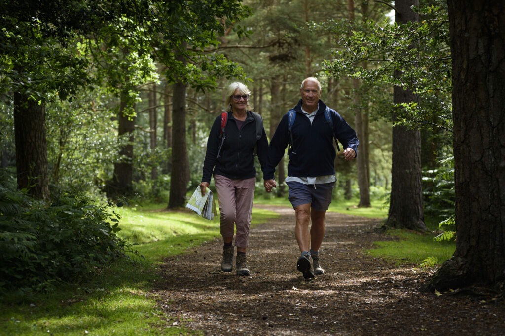two older people holding hands walking along a forest track
