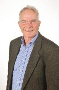 head & shoulders of a man in a grey jacket and blue shirt