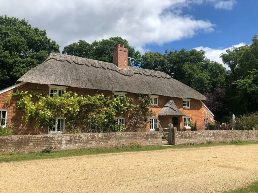 A red brick thatched cottage with yellow climbing roses and a gravel path in front