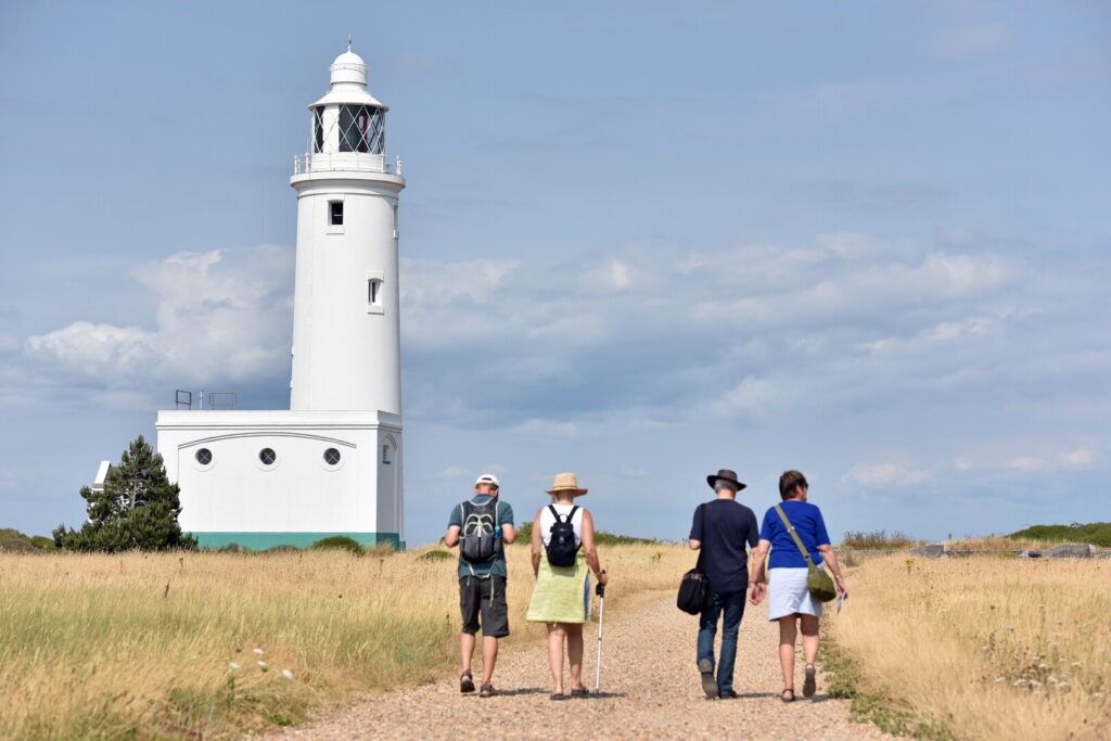 Four people walking up a path between grass with a white lighthouse at the side