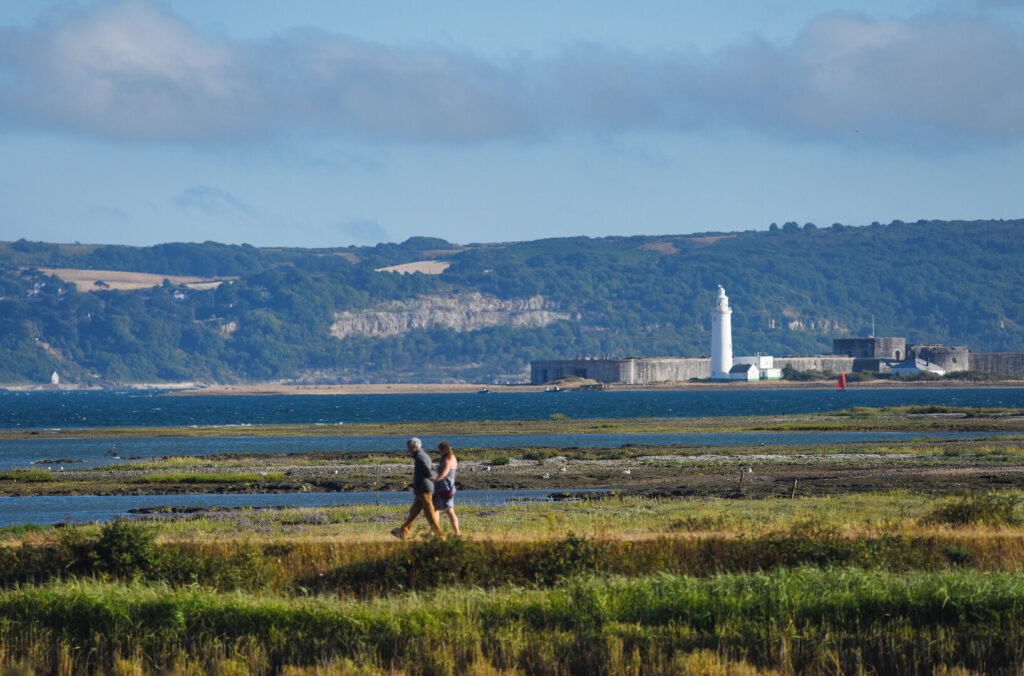 Two walkers with the sea and lighthouse behind
