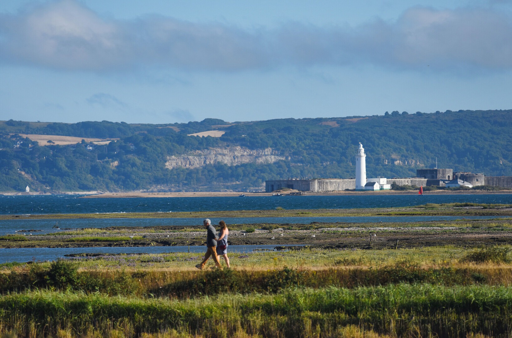 Two walkers with the sea and lighthouse behind