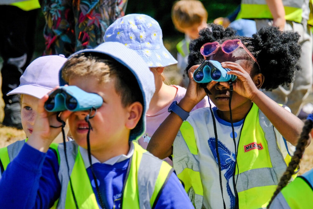 A group of children with binoculars wearing high vis vests