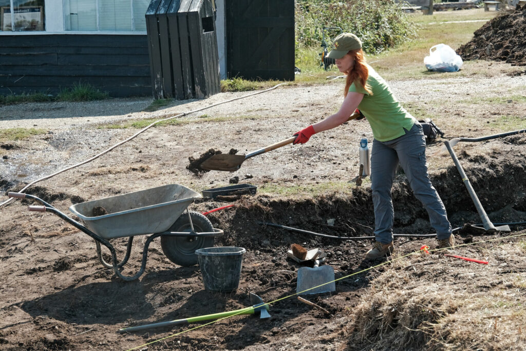 A person shovelling mud into a wheelbarrow