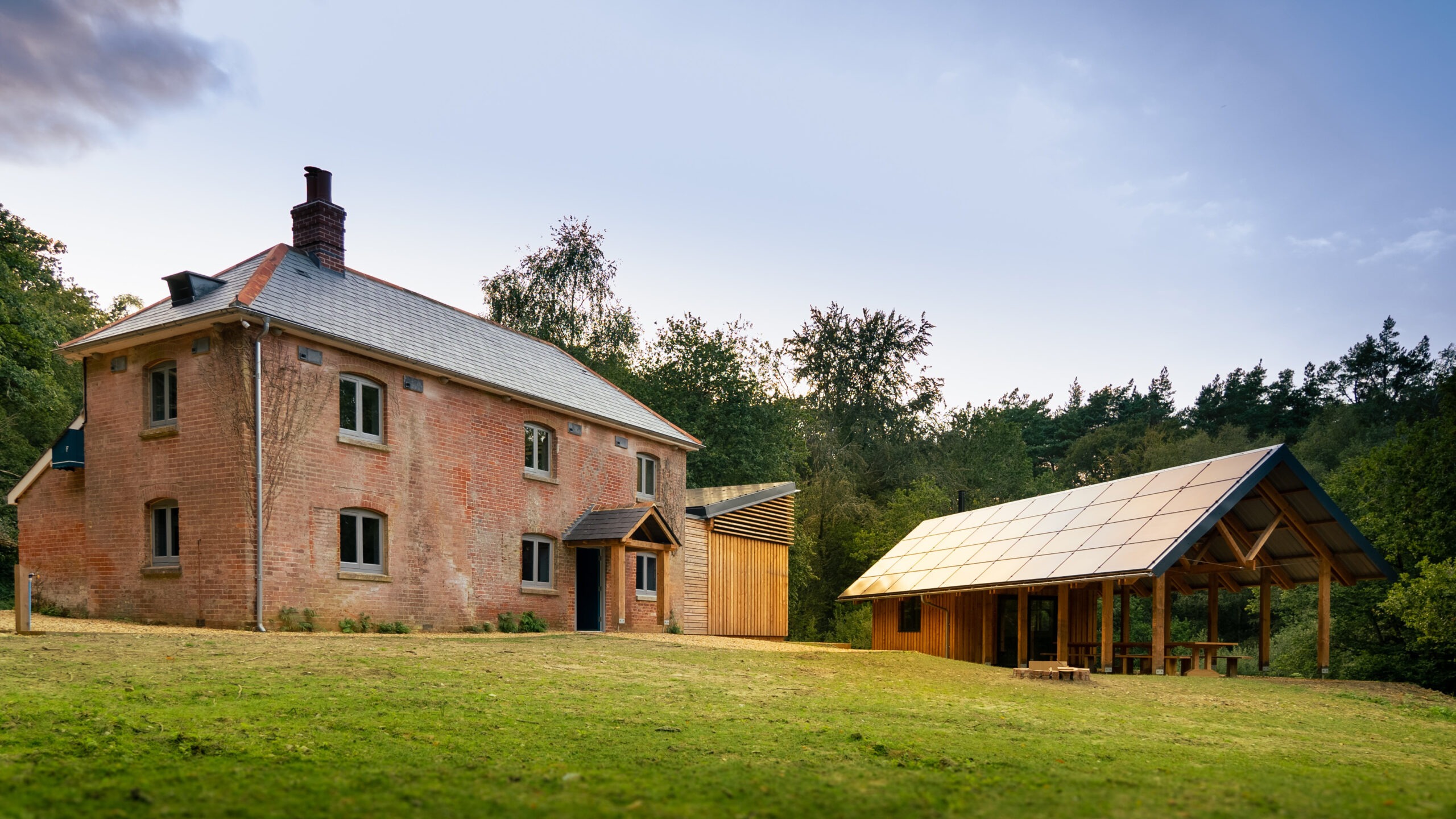 An older style cottage with a wooden outbuilding in front of woodland