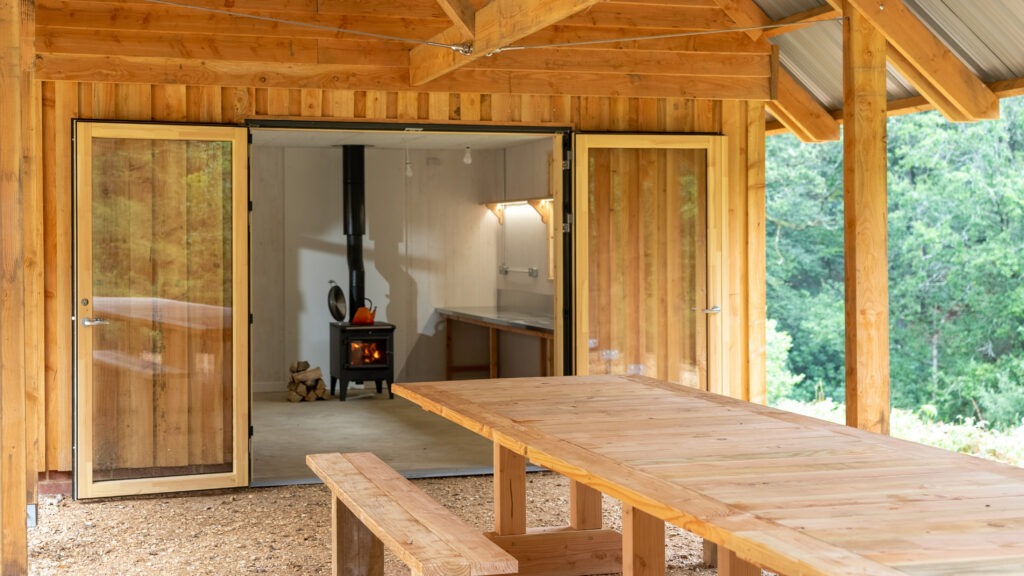 A wooden cabin with a wood burning stove and an outdoor table