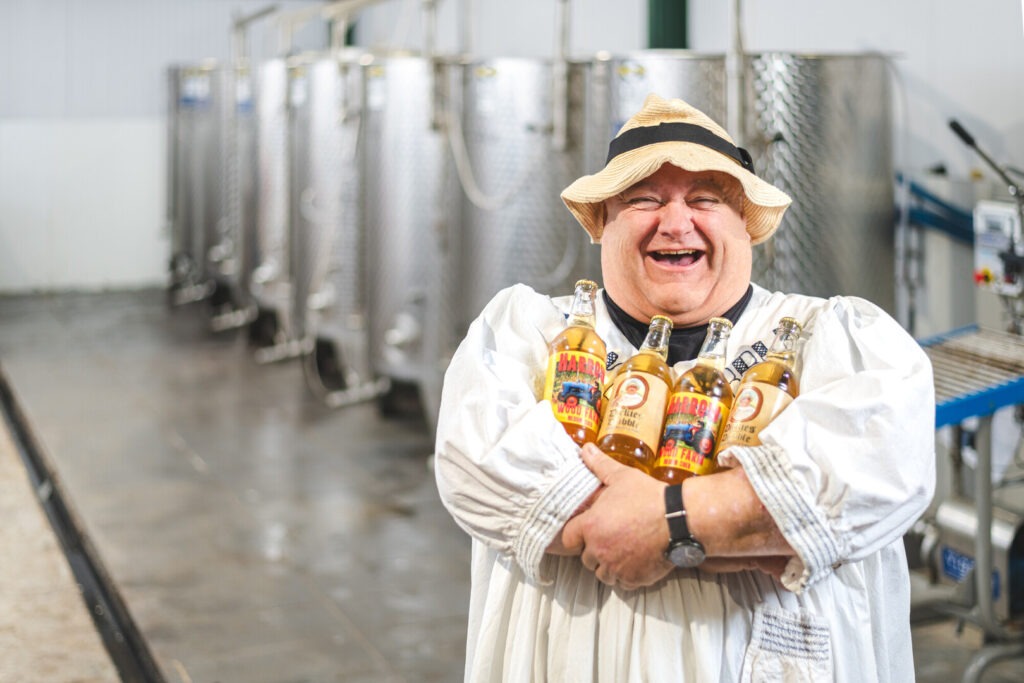 Man in a brewery laughing holding bottles of cider