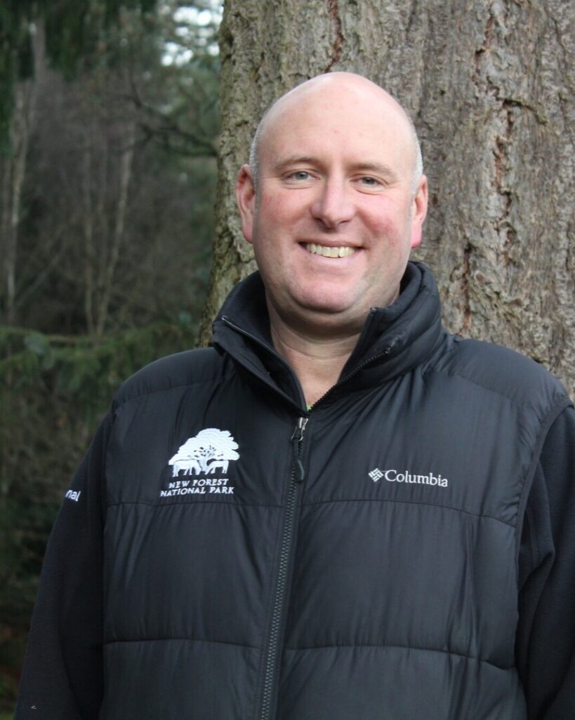 a person wearing a black gilet with a tree behind him