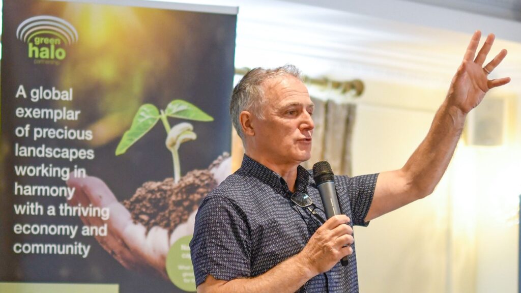 a person with a microphone talking to a conference with a banner saying Green Halo behind