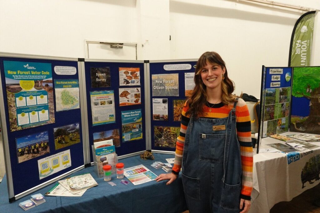 A person standing in front of an information stand in a village hall.