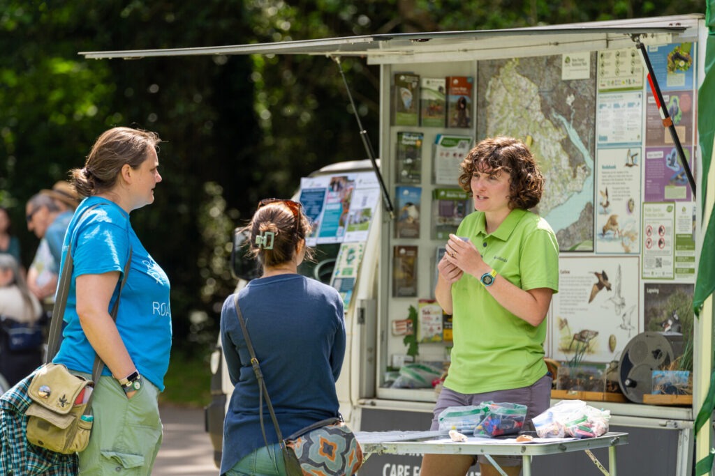 a ranger talking to two people with an information van behind