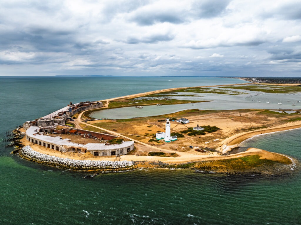 Aerial view of Hurst Castle and lighthouse on a narrow shingle spit, with sea on both sides under cloudy sky