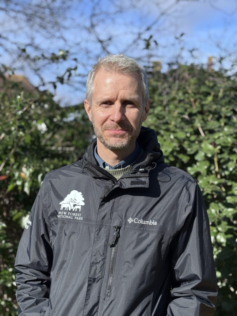 A person in a black jacket with trees behind