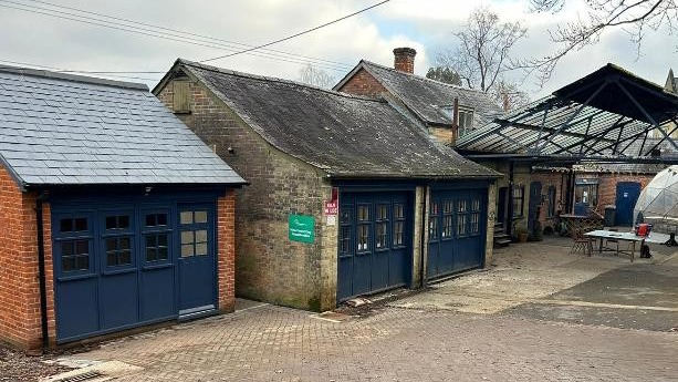 Minstead Trust toilet block building with blue double doors and slate roof, beside a covered walkway and outdoor seating area