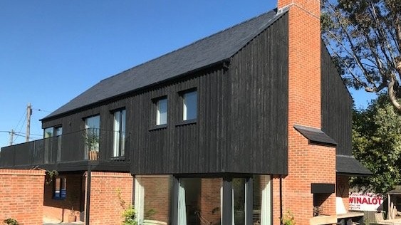 Modern black timber and brick building with pitched roof and large windows, viewed from street in Lyndhurst