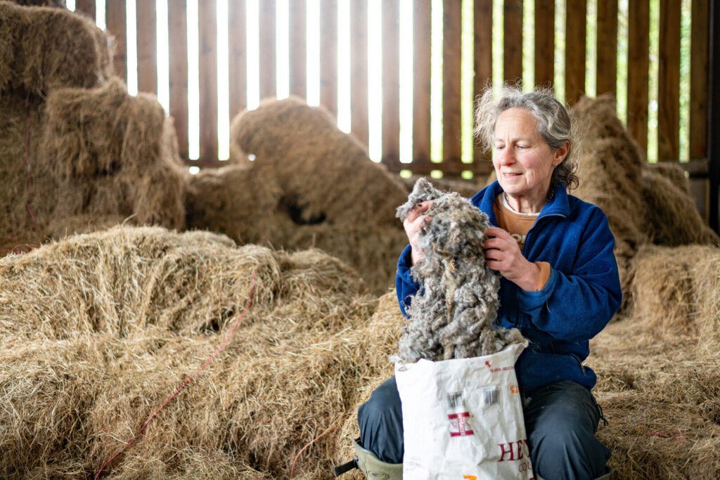 Farmer sitting amongst hay examining bag of wool