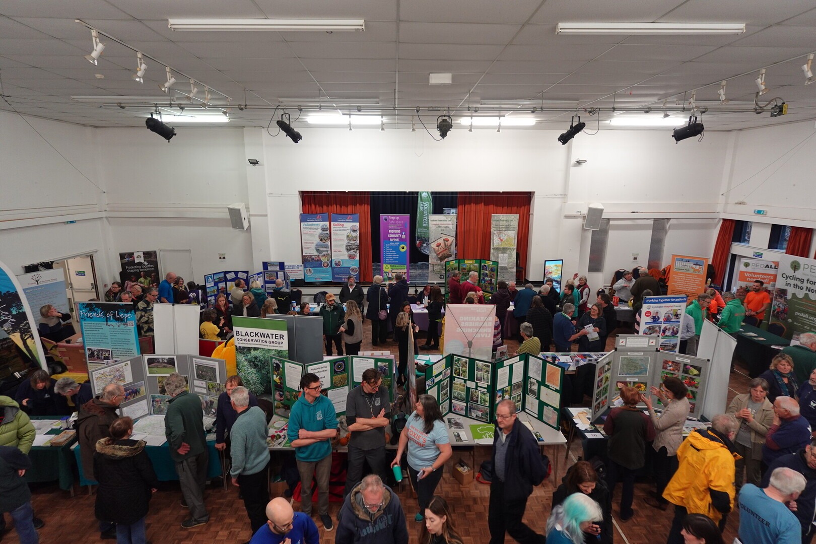 A crowd in a community hall surrounded by stalls for the New Forest National Park Volunteer Fair.