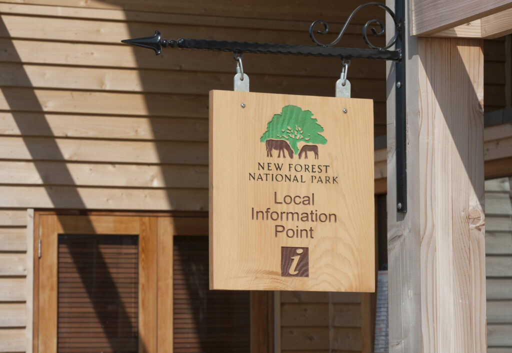 Wooden hanging sign reading New Forest National Park Local Information Point with tree and ponies logo on a timber building