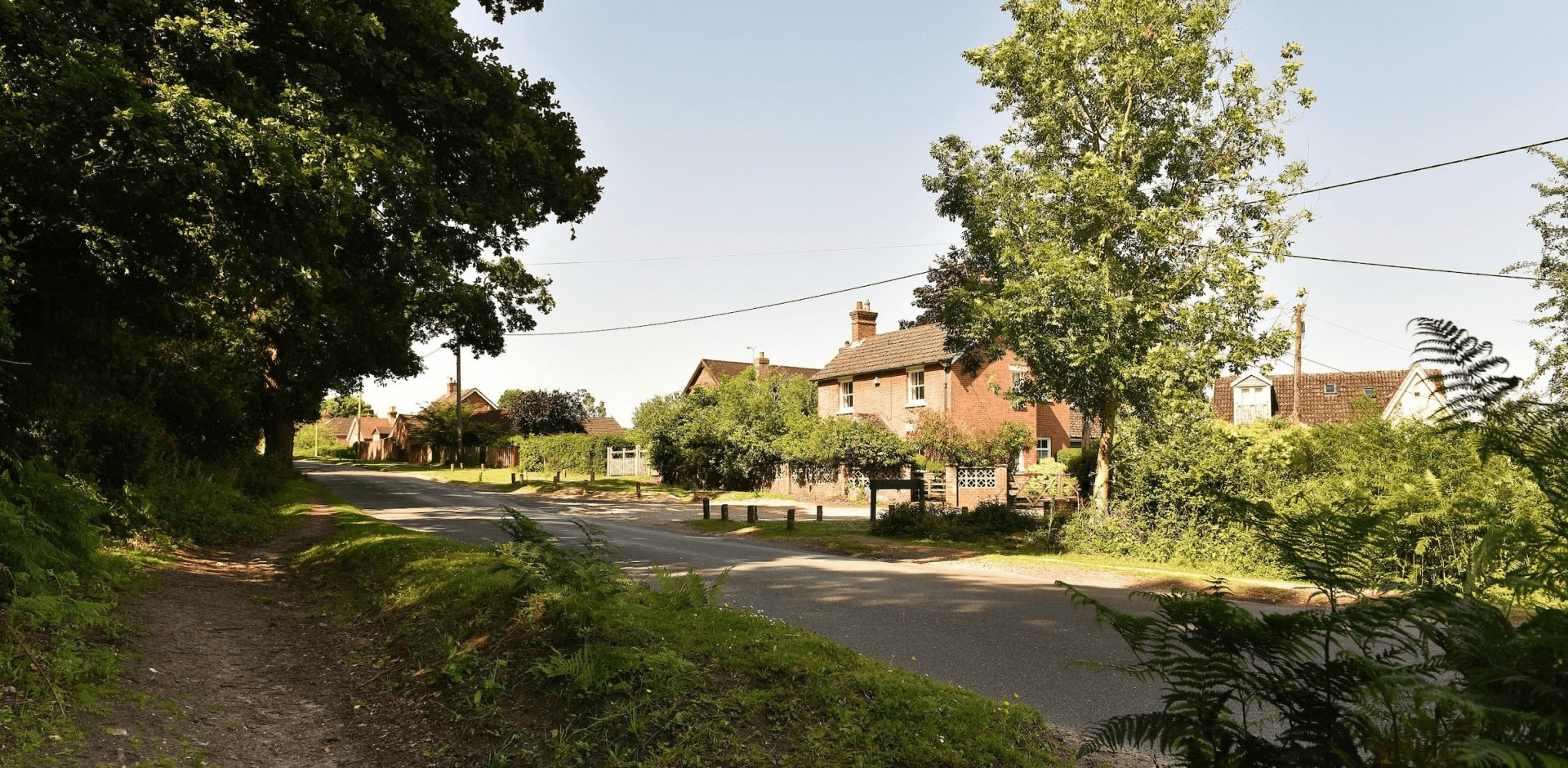 Quiet country lane with trees and footpath, passing brick houses and hedges in a village near Wiltshire and the New Forest