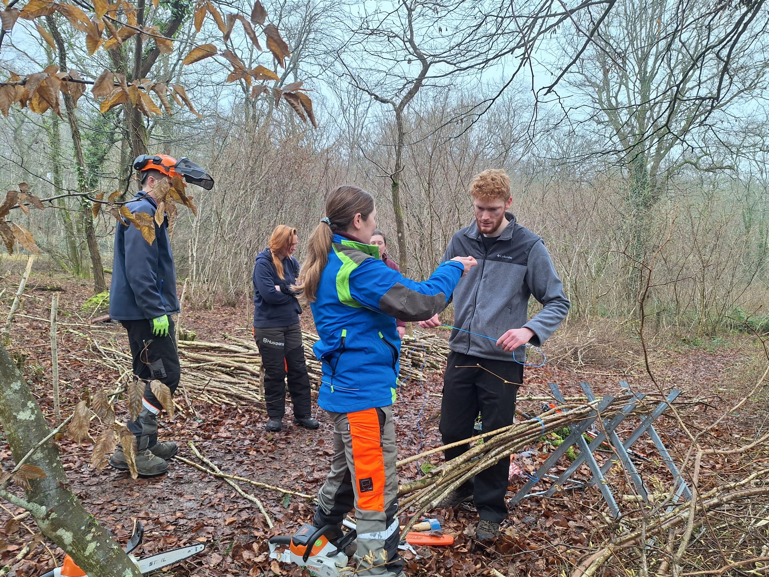CET Operations Manager Anna Barnard teaching Intern Charlie how to tie up bundles of coppiced hazel