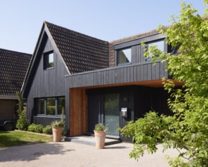 Modern black-clad house extension with pitched tiled roof, large windows, and recessed entry marked number 8 with potted plants
