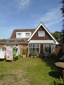 Rear of house at 8 Moorlands Close, Brockenhurst, with conservatory, lawn, clothesline with laundry, and potted plants