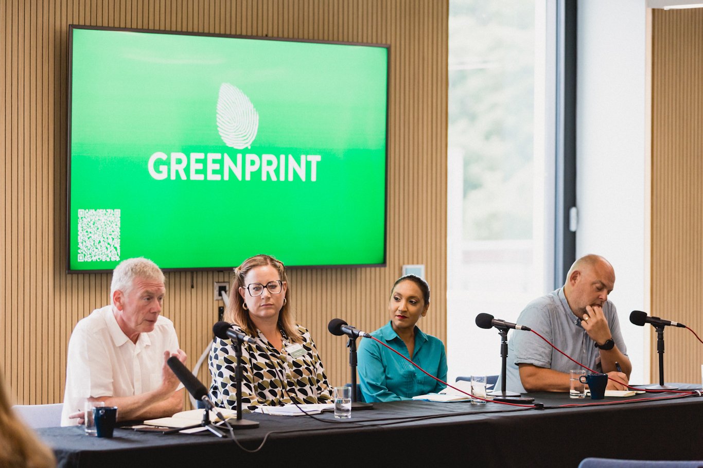 Panellists seated at a table with microphones and Greenprint on a screen behind