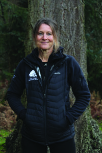East area ranger Naomi Addleton standing in woodland, wearing a New Forest National Park jacket with hands in pockets
