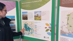 Person pointing at a map on a planning poster titled “Natural environment of the National Park” displayed on green boards