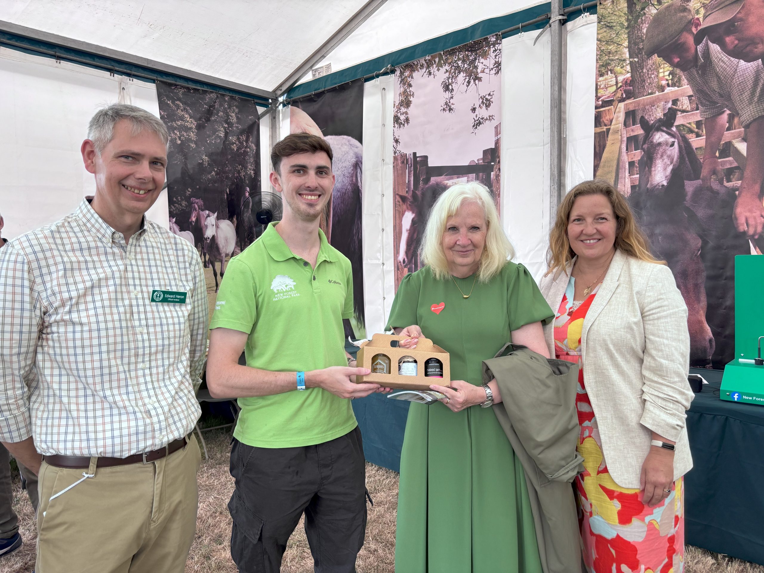 Four people holding a presentation pack of jam in a tent