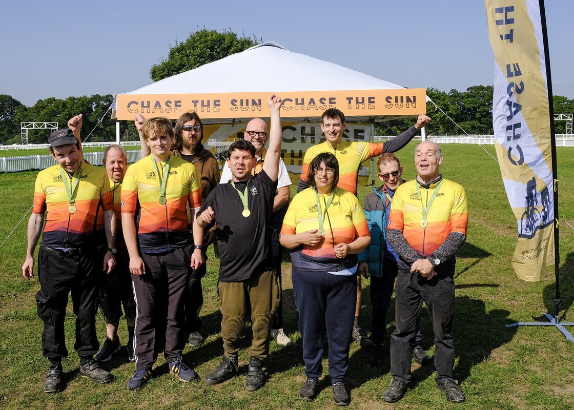 Chase the Sun founder Olly Moore and Minstead Trust all wearing Chase the Sun jerseys and Pass the PEDALL medals, they are all cheering with arms in the air