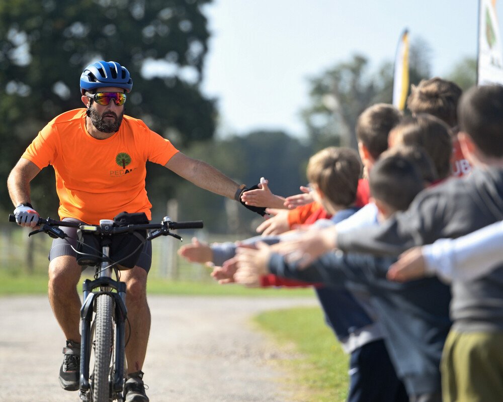 PEDALL Operational Lead Gareth Jones high-fiving a group of school children as he cycles past