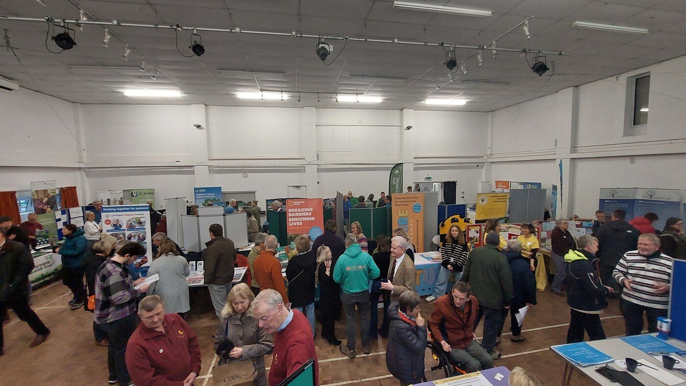 A busy village hall full of information stalls with people mingling and chatting