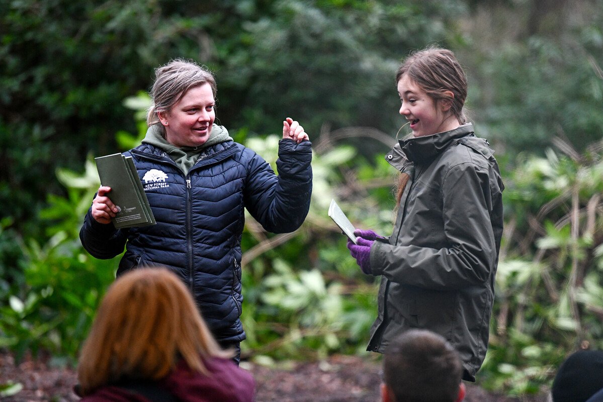 A New Forest Junior Ranger receiving a logbook at an awards session in a woodland setting. She is very happy