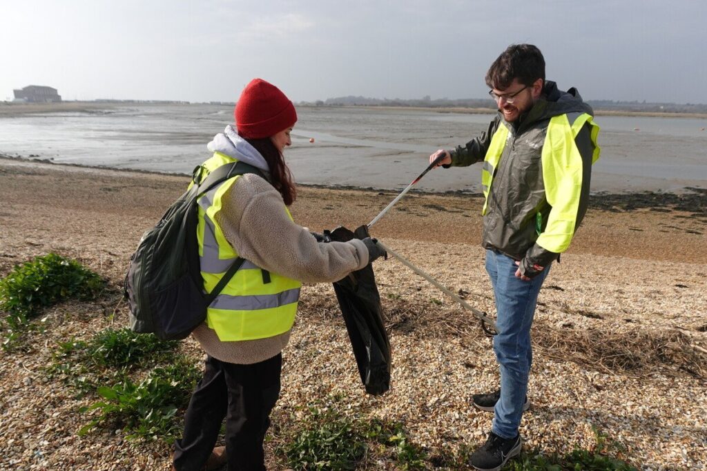 A man and a woman in high-vis litter picking on a beach