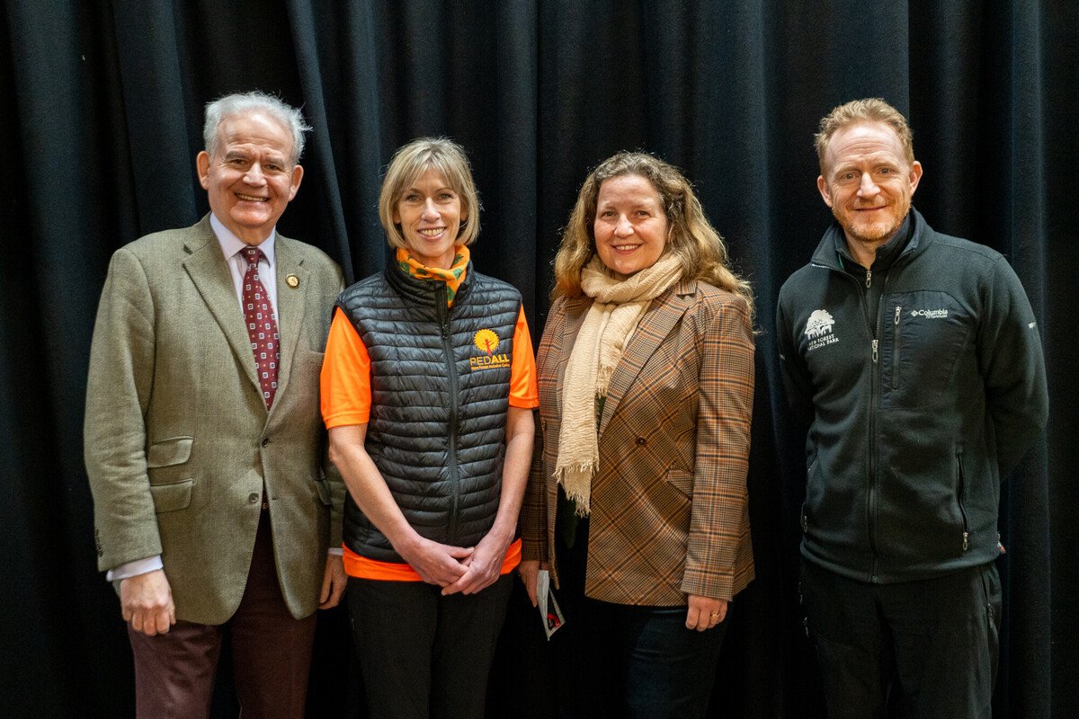 Four people stood on a stage against a black curtain. Left to right: New Forest East MP Sir Julian Lewis, PEDALL New Forest Inclusive Cycling manager Shelley Filby, New Forest National Park Authority CEO Alison Barnes and NPA Access and Learning Manager Jim Mitchell