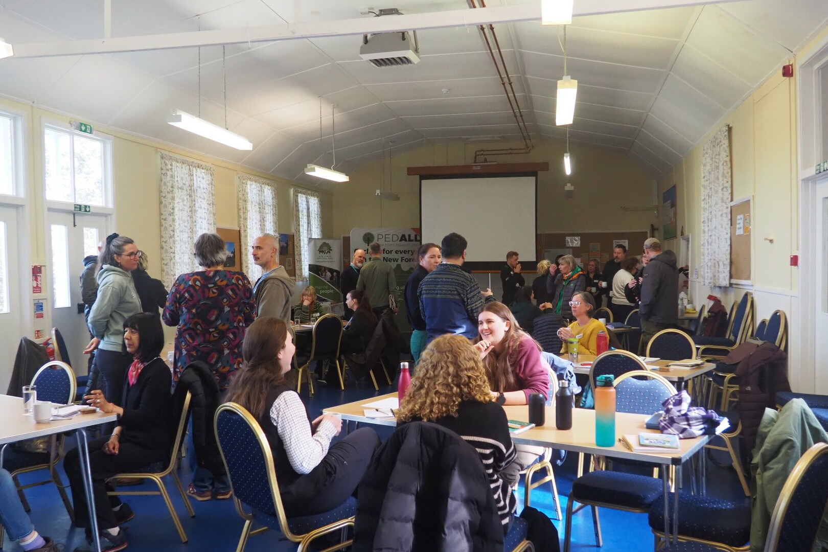 People gather in a room to discuss wellbeing in the New Forest. Some are standing and others are sitting.