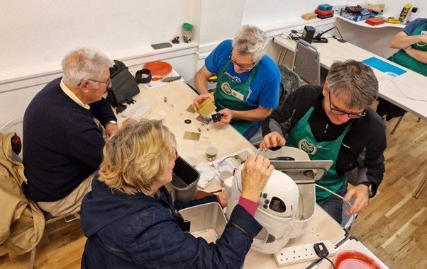 Volunteers at a repair cafe work on a kitchen appliance and small electronics around a table