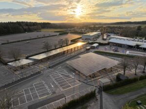 Aerial view of solar panel carport canopies over Paultons Park parking lot at sunset, with park buildings and rides in distance