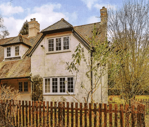 an old detached cottage with a wooden fence in front
